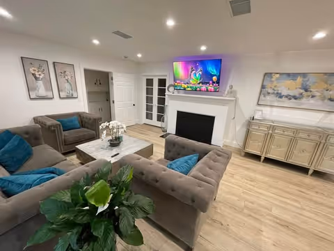 Cozy common living room with couches, a fireplace, TV, and plants.