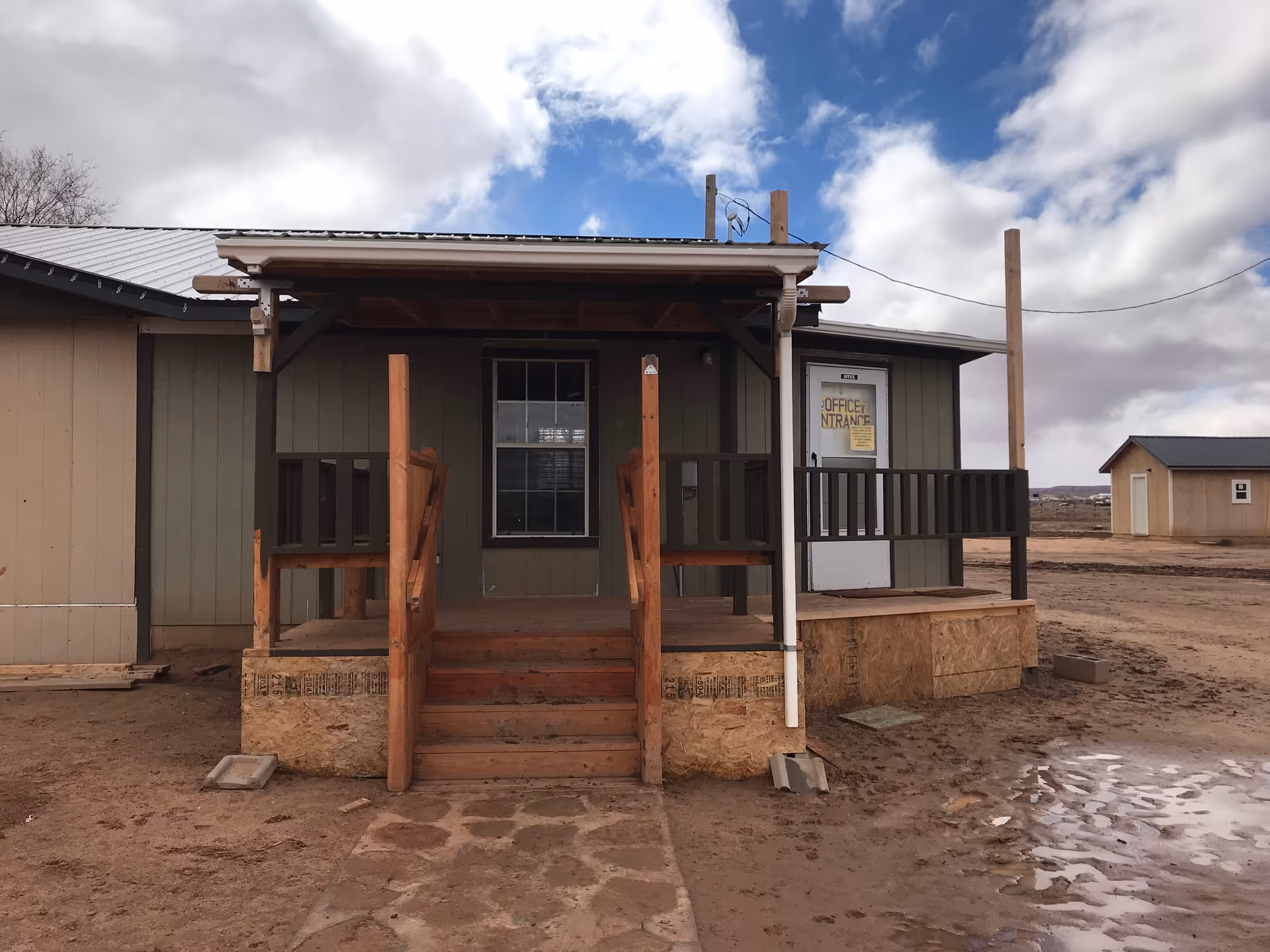 Front of a small building with a wooden porch and office entrance sign.