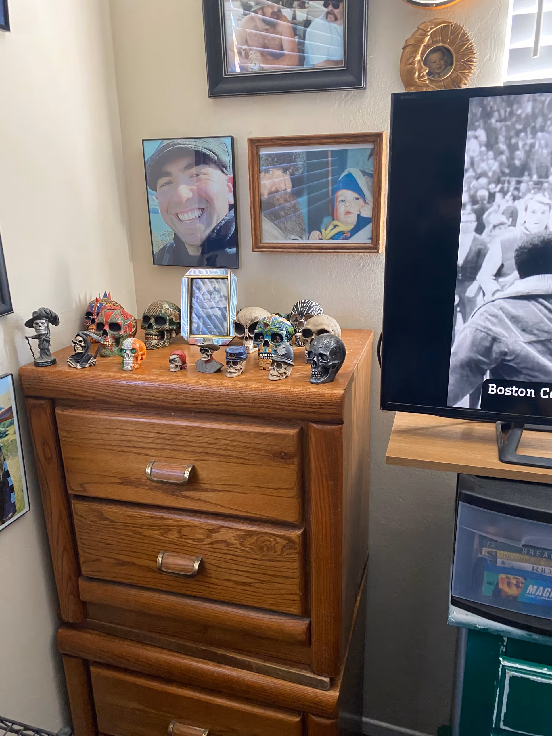 Wooden dresser topped with skull sculptures and framed photos, with a TV visible nearby.
