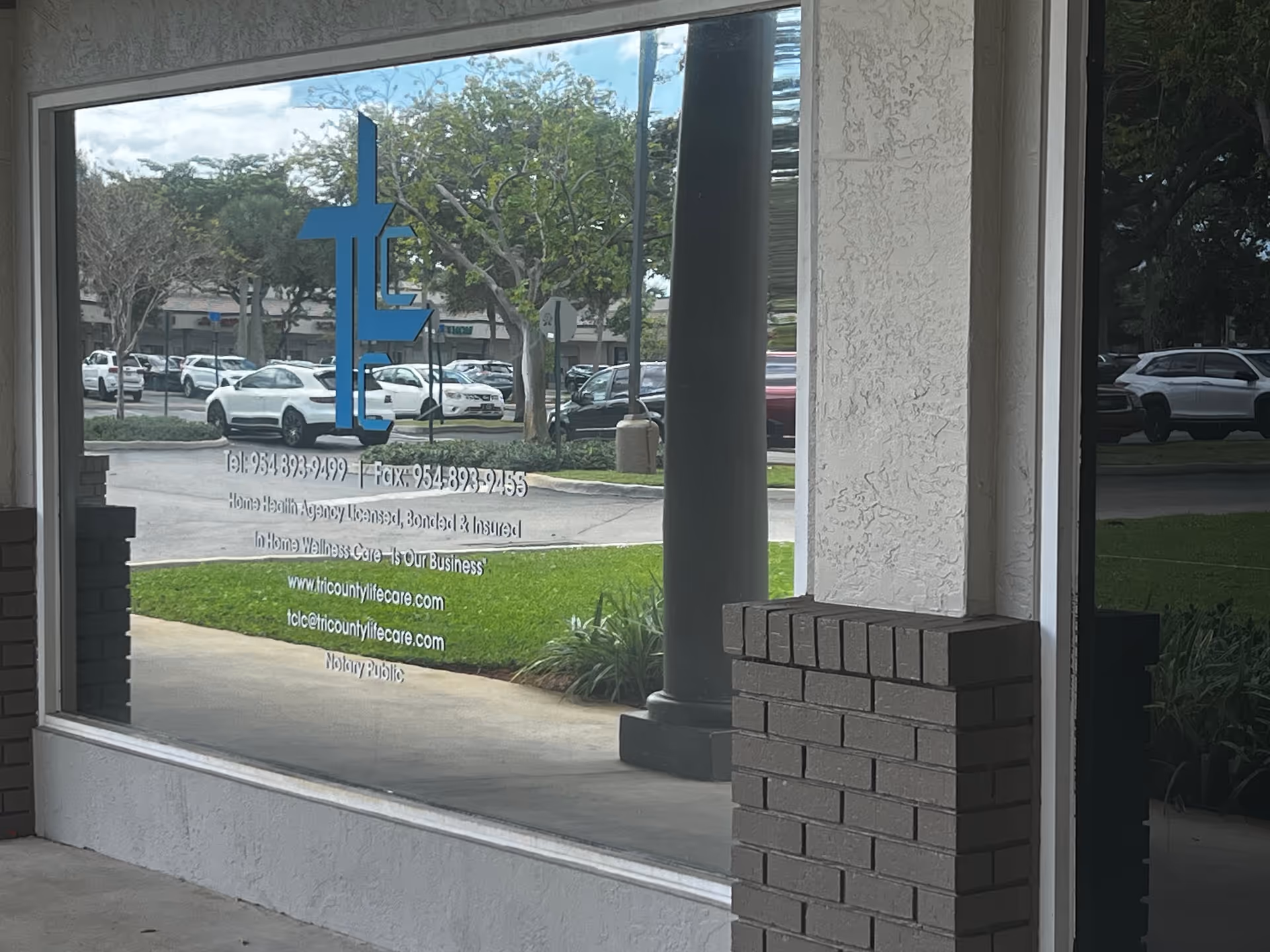 Front of Tri-County Life Care building visible through glass window with blue logo and parked cars.