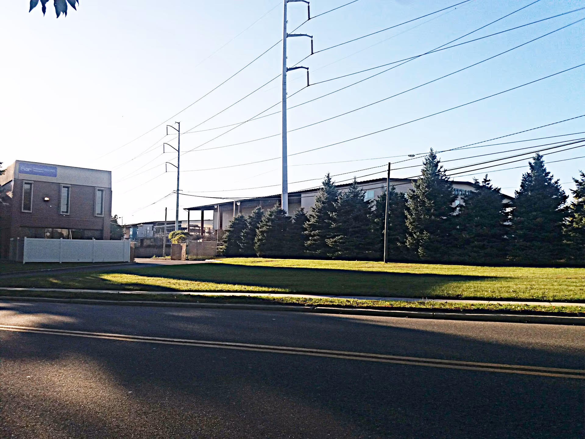 Exterior view of a medical facility with trees, fence, and utility poles along a street.