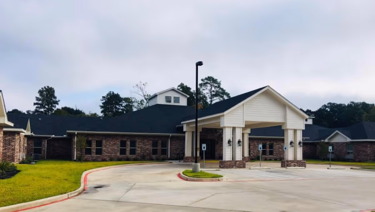Single-story brick building with a covered entrance/porte-cochère and circular driveway under an overcast sky.