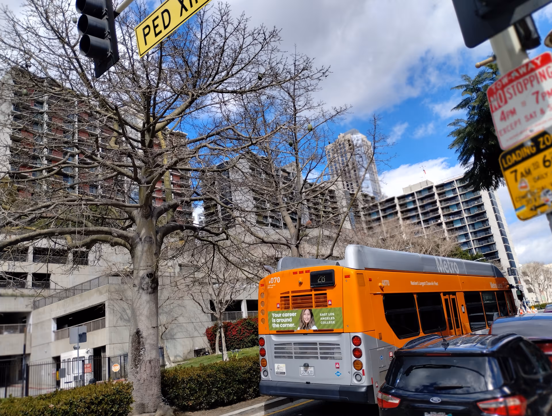 An orange city bus on a street with leafless trees and tall buildings.