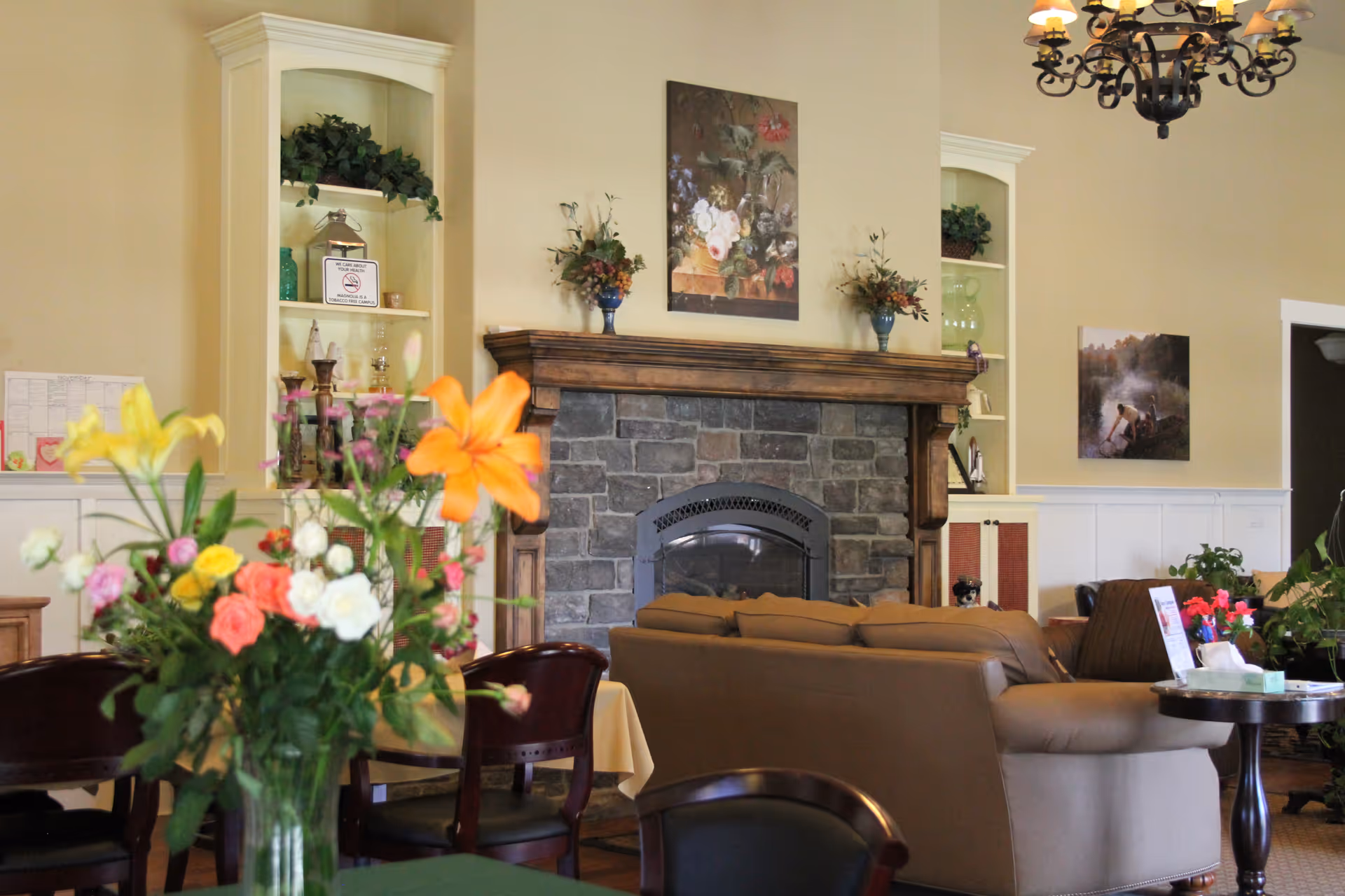 Cozy senior living lounge with a stone fireplace, seating, and colorful flower arrangements.
