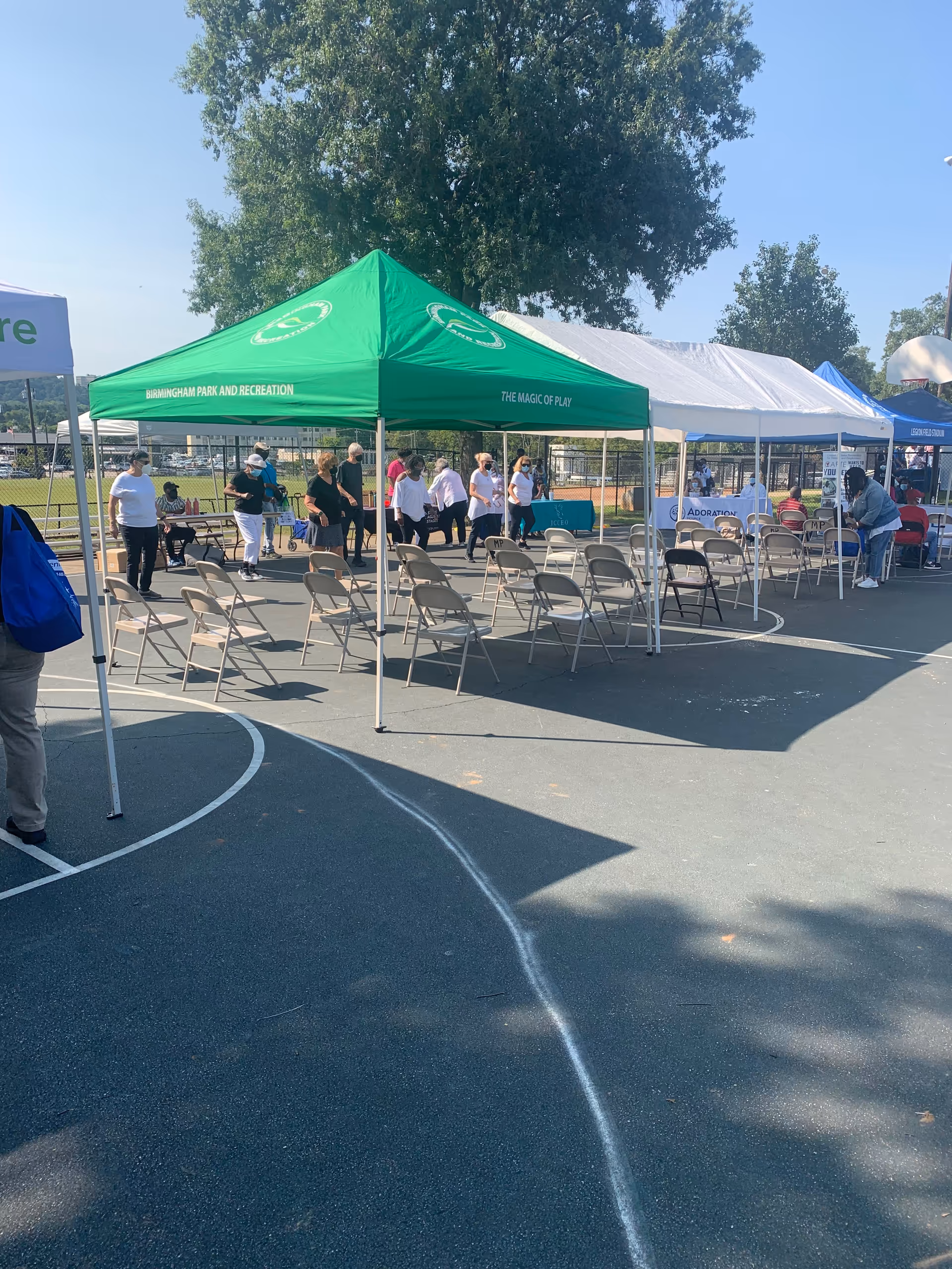 Outdoor event with green and white tents, folding chairs, and people in a parking lot.