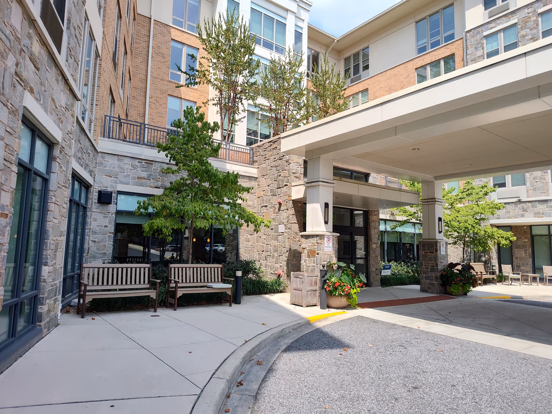 Courtyard exterior of a senior living facility with benches, trees, and a covered entrance.