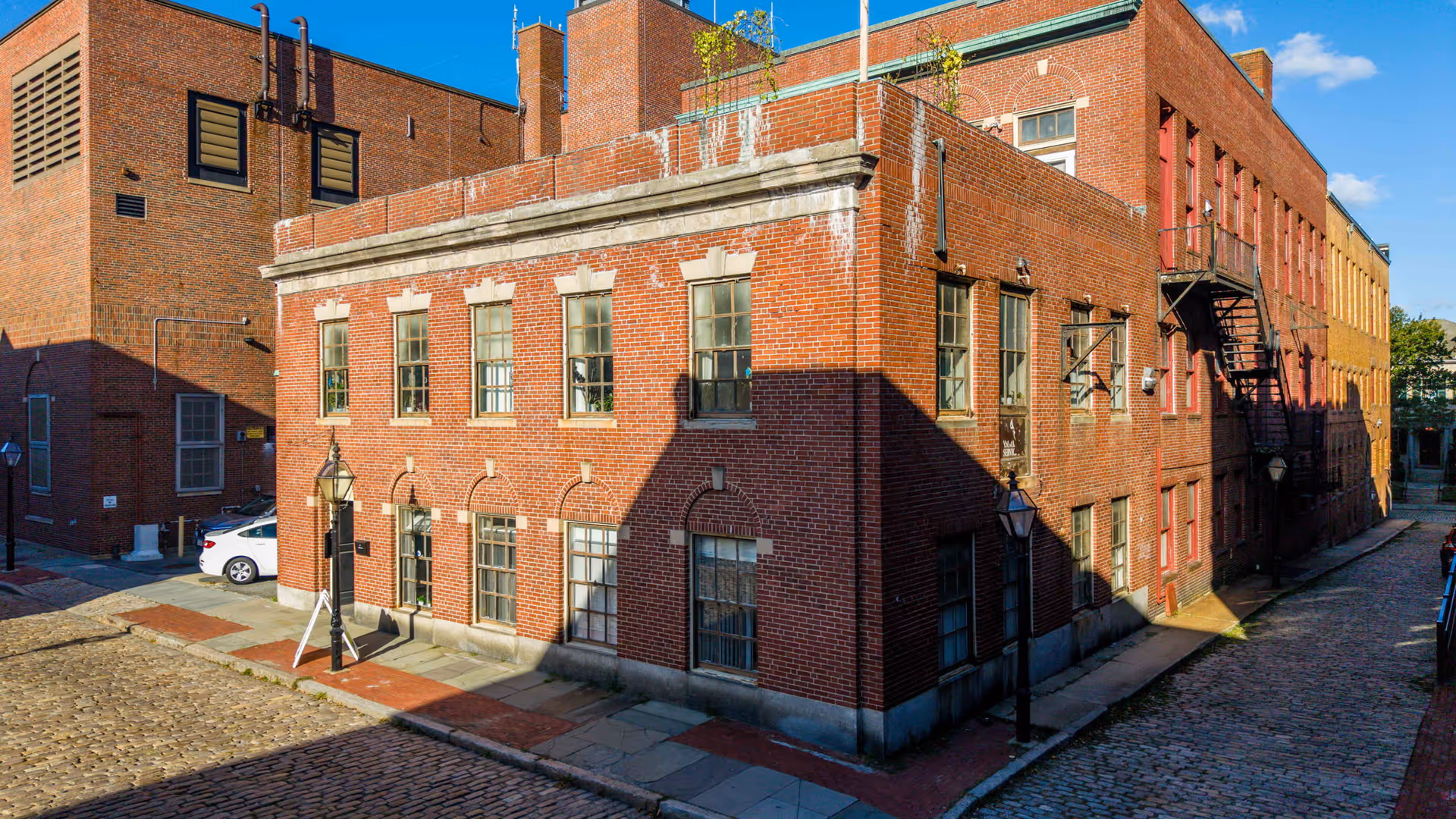 Historic brick corner building along a cobblestone street with lampposts.