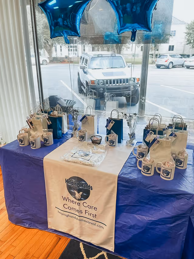 Indoor display table with gift bags, mugs, and a Helping Hands banner inside a care facility.