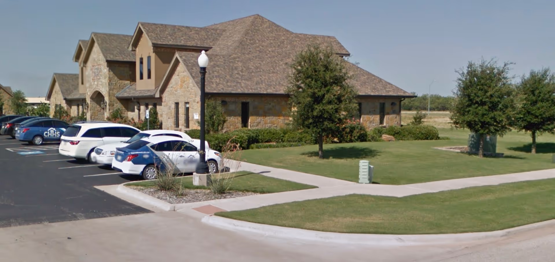 Stone-clad senior facility with a parking lot, manicured lawn, and trees in front.