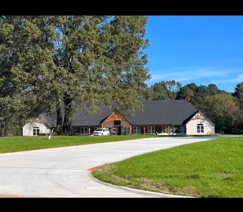 Exterior view of a single-story assisted living facility with a curved driveway and trees.