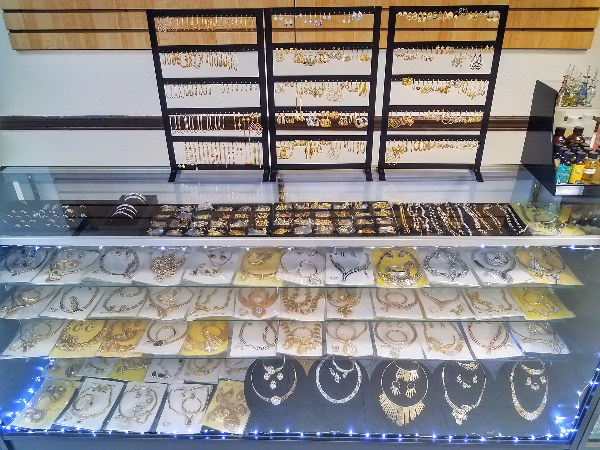 Glass jewelry display case with rings, necklaces, and bracelets arranged on trays.