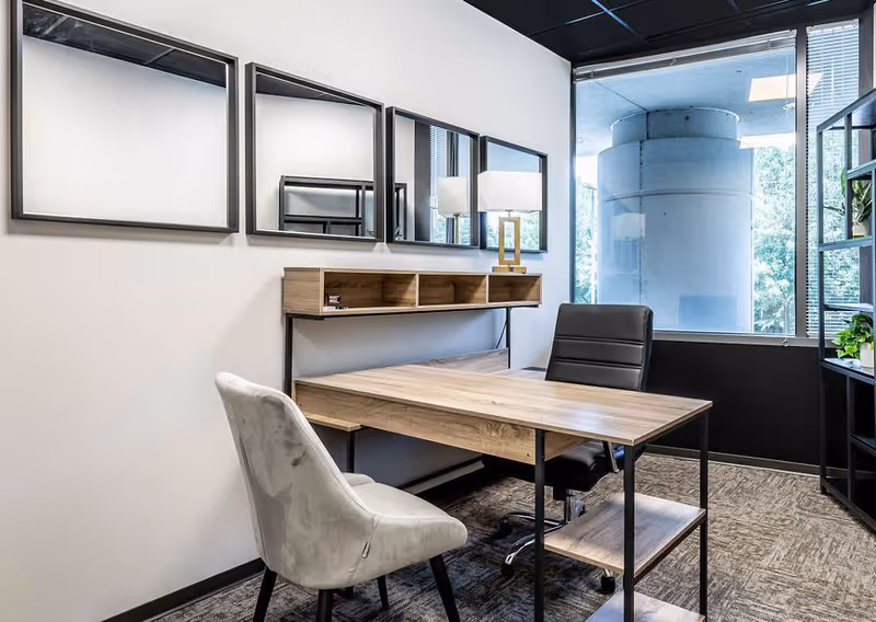 Modern office in a facility with a wooden desk, chairs, wall shelves, and a large window.
