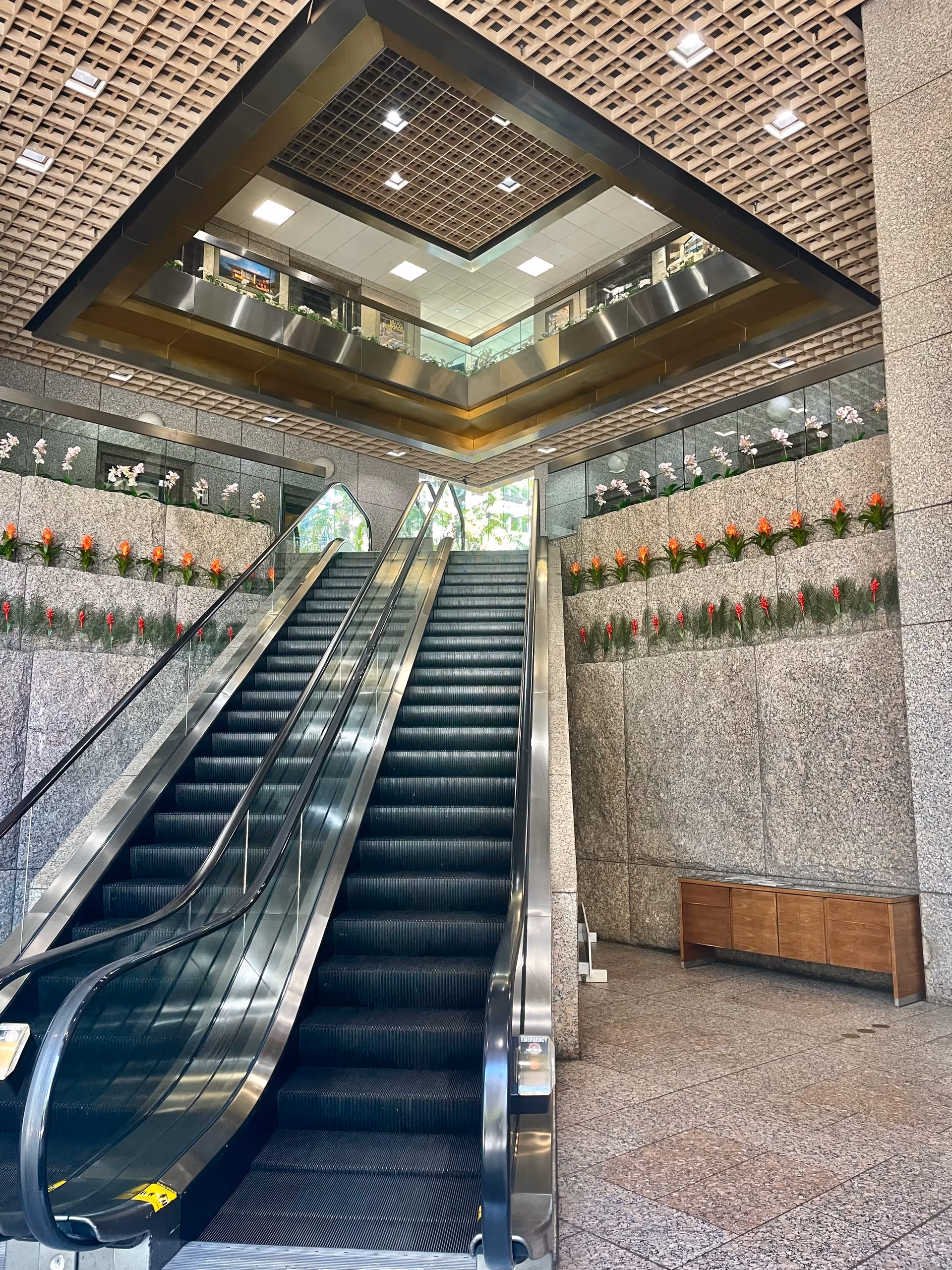 Indoor atrium featuring escalators, marble walls, and flower decorations along the sides.