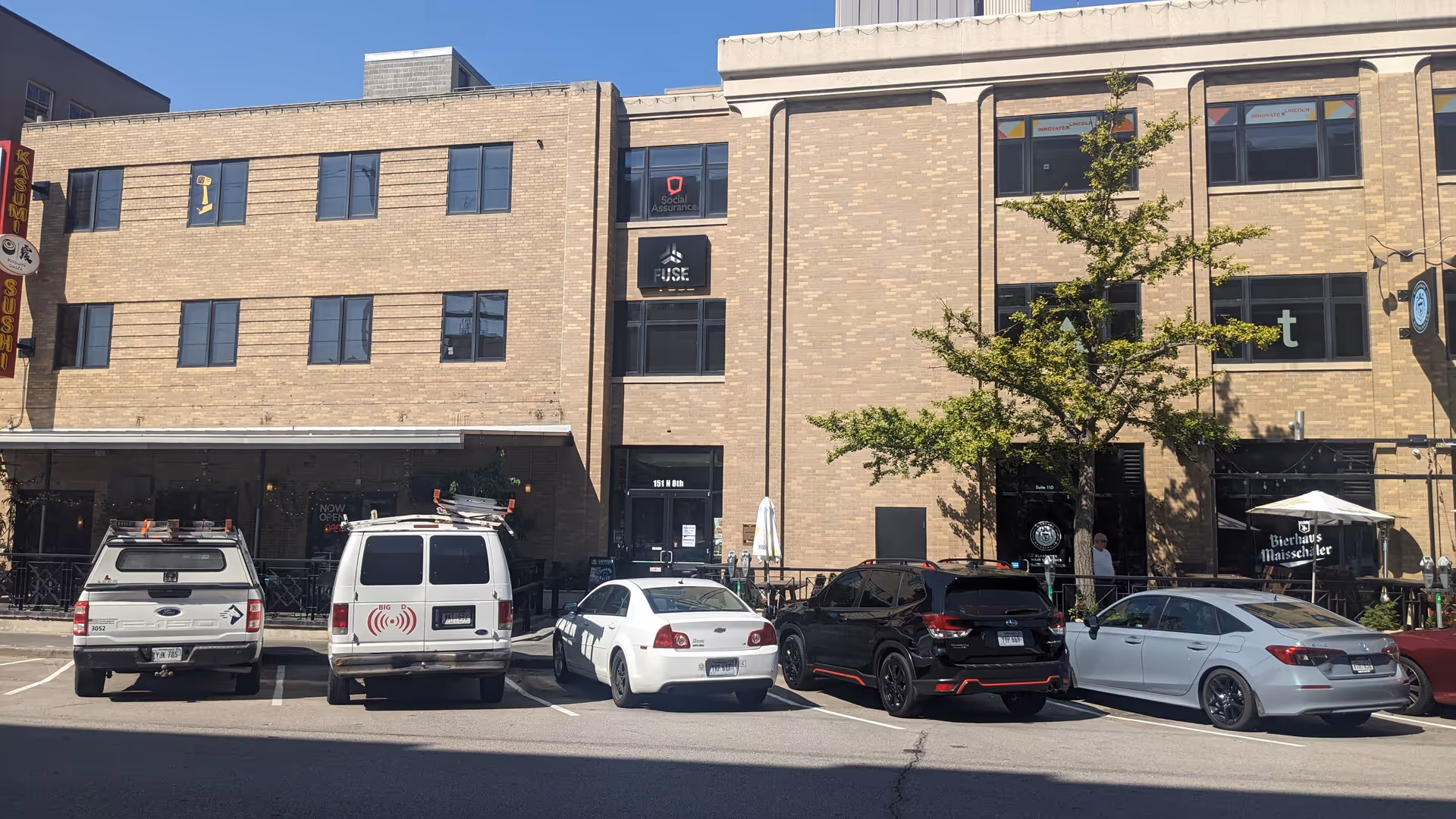 Exterior of a brick, multi-story building with several parked cars along the street.