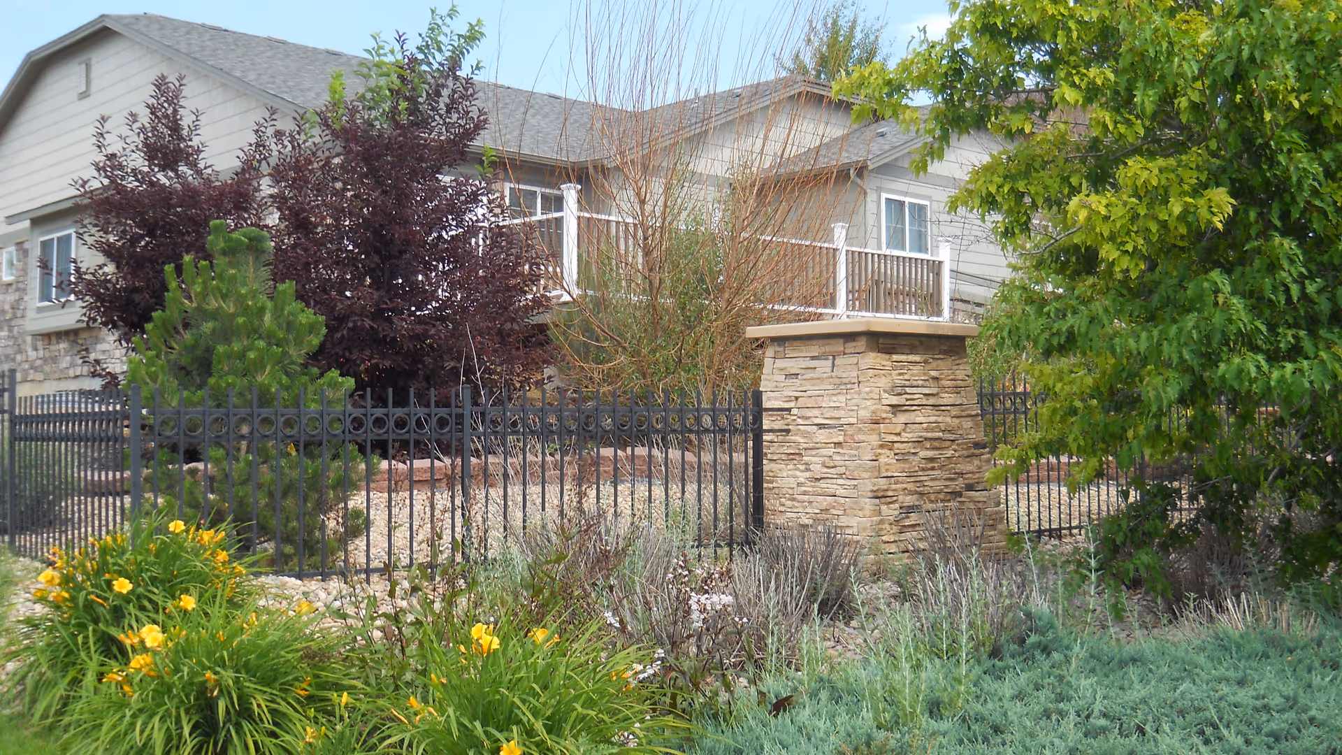 Front exterior of Cardan Manor Assisted Living with stone pillar, fence, and landscaping