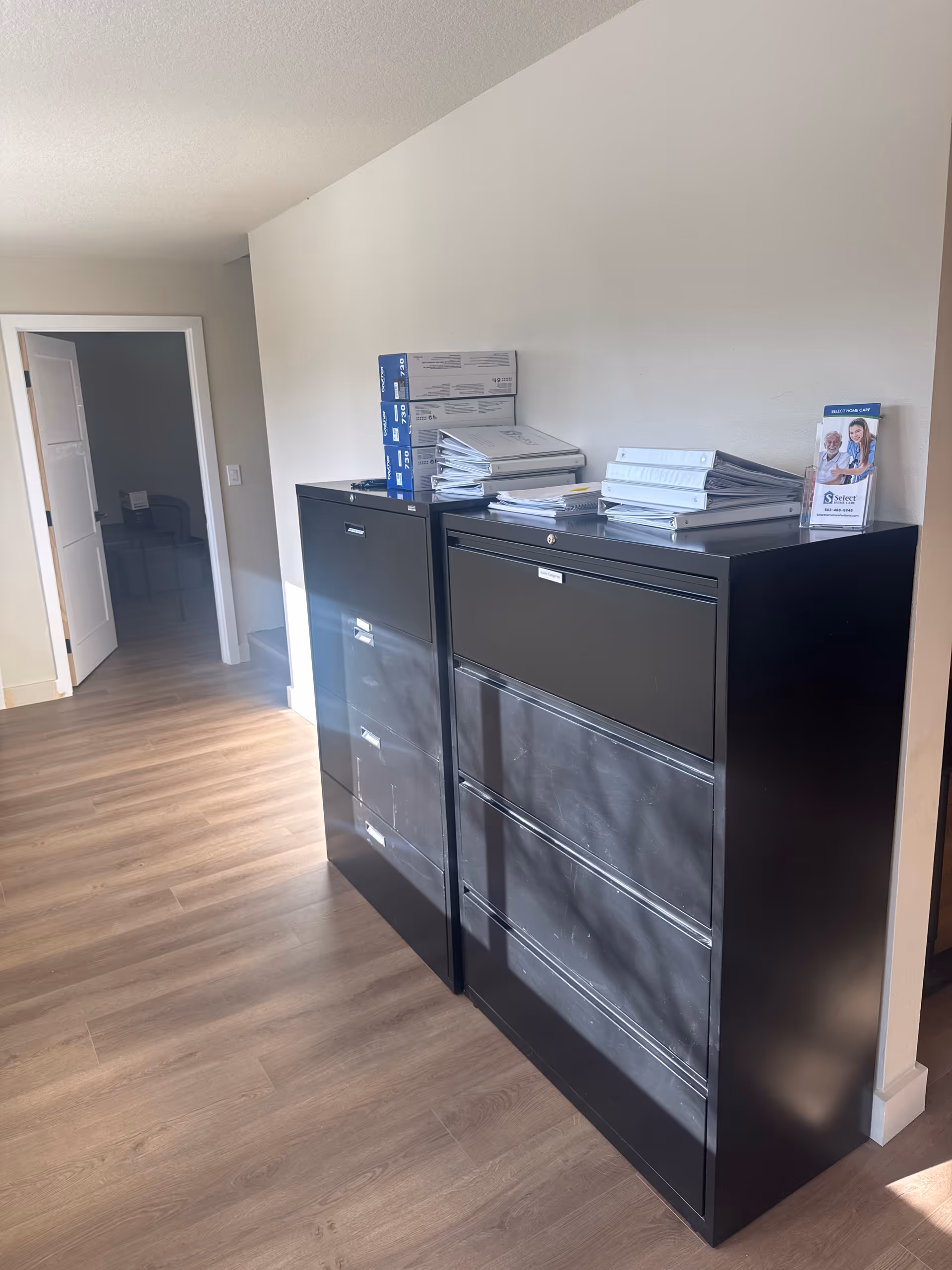 Two black filing cabinets with stacks of documents in a hallway office area.