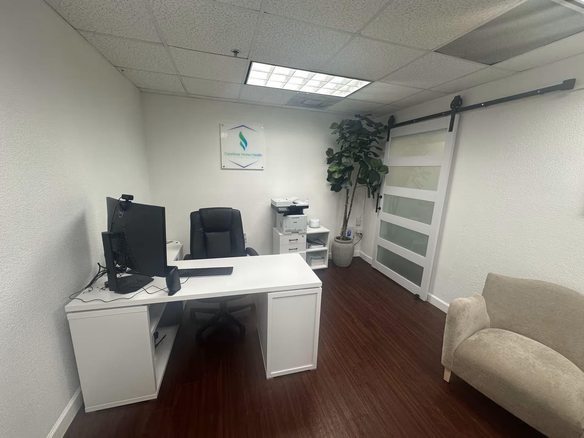 Office space inside CareNow Home Health with desk, computer, printer, and couch.