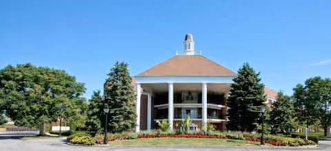 Front view of a round, columned facility entrance with manicured landscaping.
