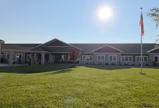 Long, single-story senior living building with a manicured lawn and flagpole.