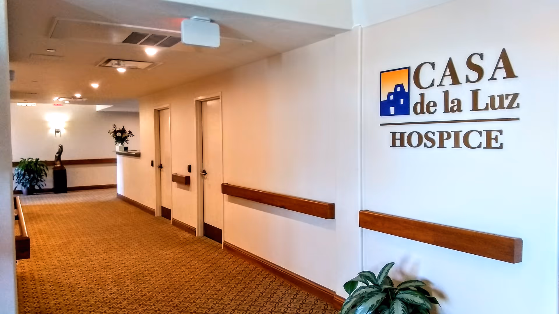 Interior hospice corridor at Casa de la Luz Hospice with doors, rails, and a wall logo.