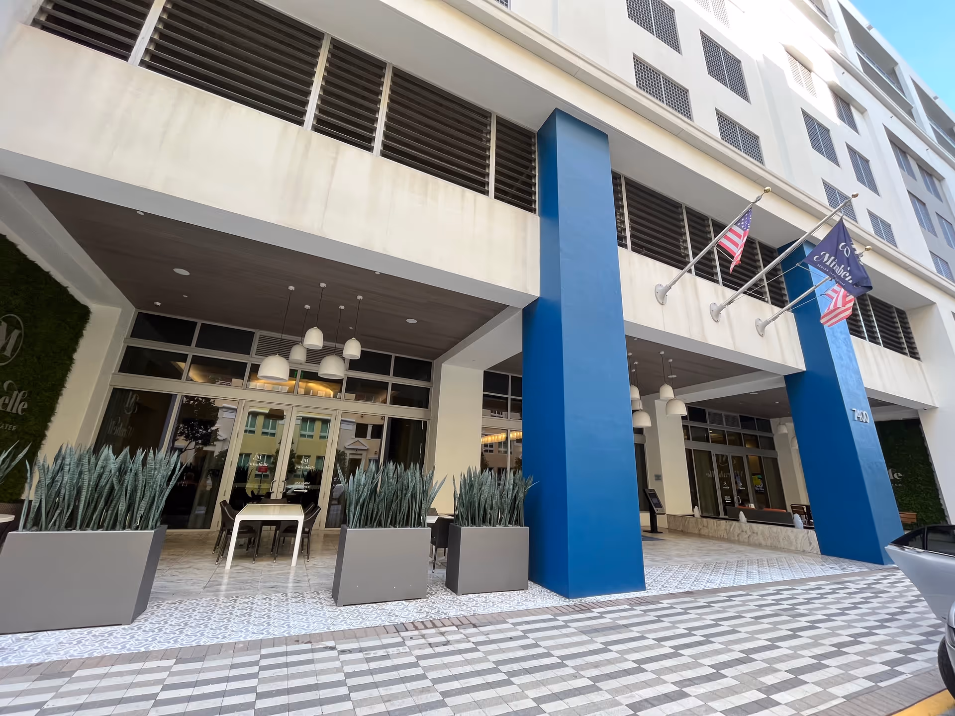 Facade of a modern senior living facility entrance with blue pillars and planters.