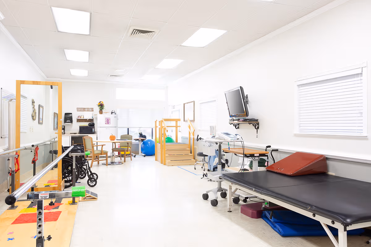 Bright rehabilitation therapy room with exercise equipment, a treatment table, and parallel bars.