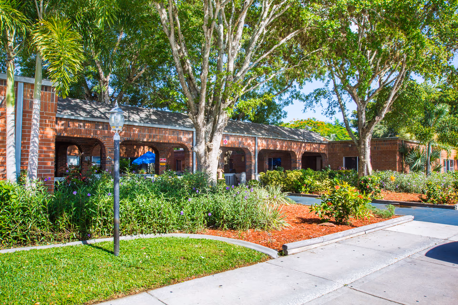 Brick building with arched walkways, greenery, and a sunny exterior.