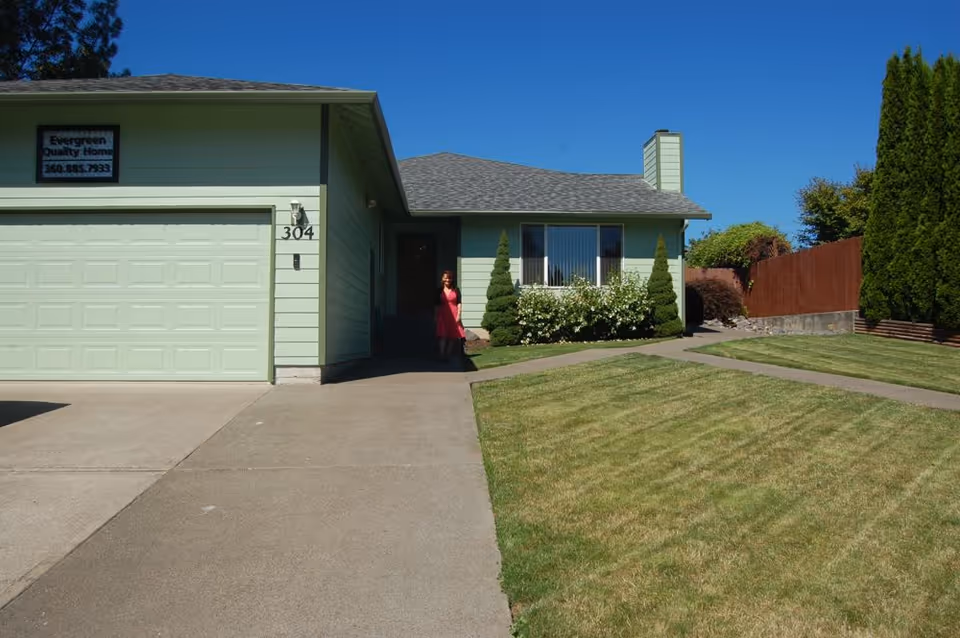 Mint-green single-story house exterior with front entry and Evergreen Quality Home sign