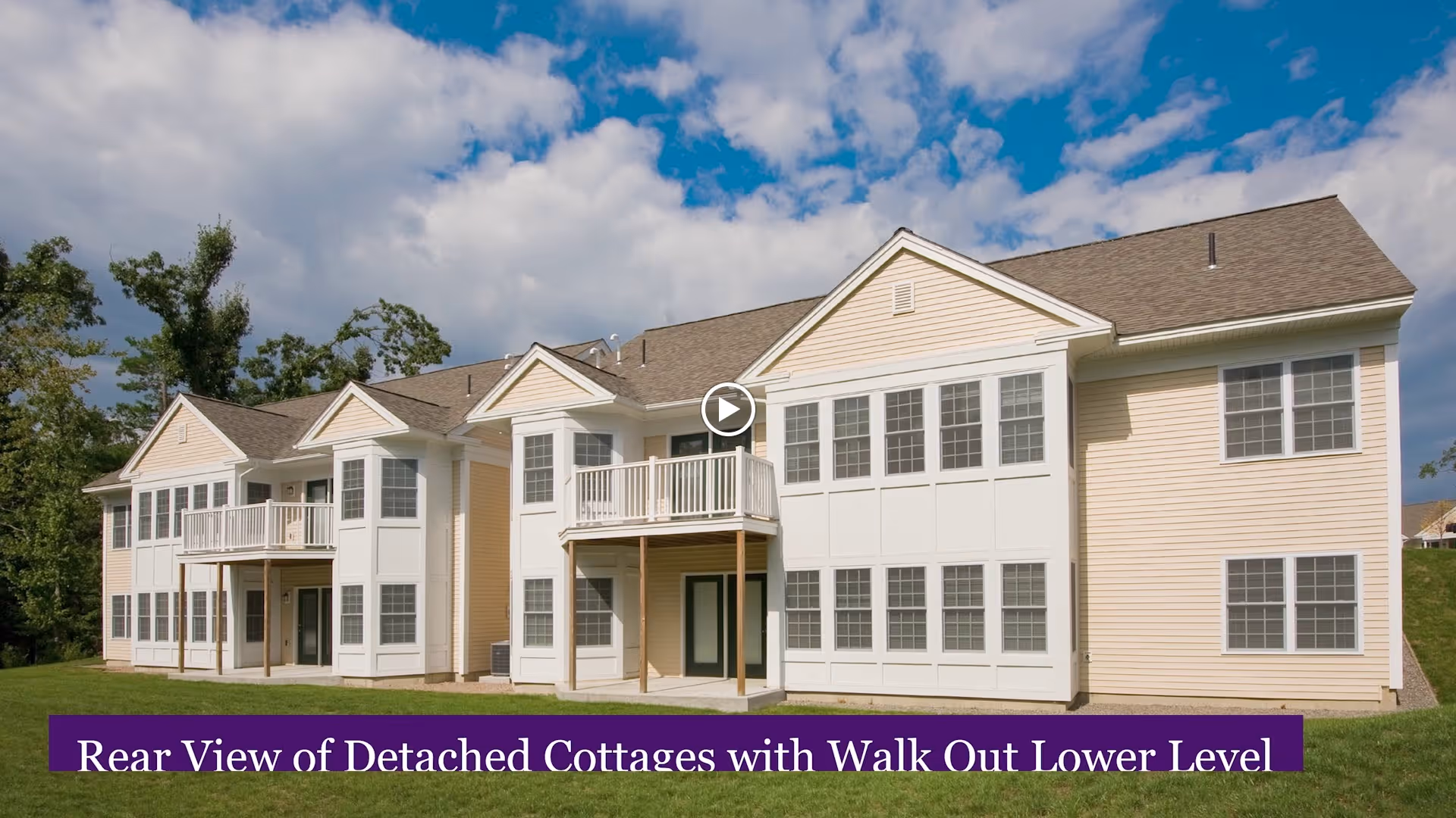 Rear view of detached cottages at The Willows Retirement Community, showing two-story buildings with multiple windows, balconies, and a walk-out lower level, under a partly cloudy sky.