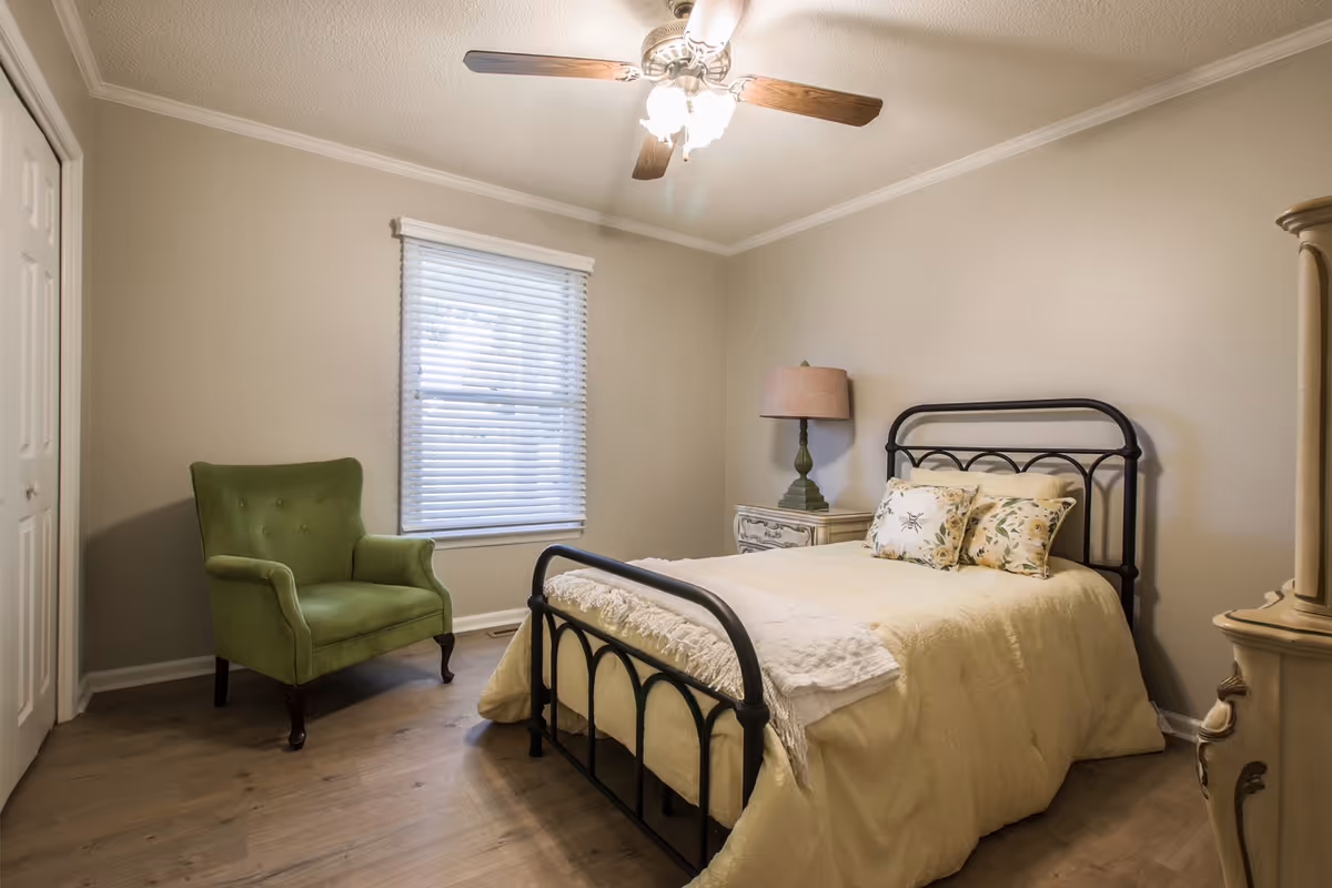 Cozy bedroom with a metal bed frame, cream bedding, green armchair, and window.