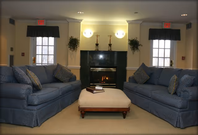 Two blue sofas flank a central ottoman in a living room with a lit fireplace.