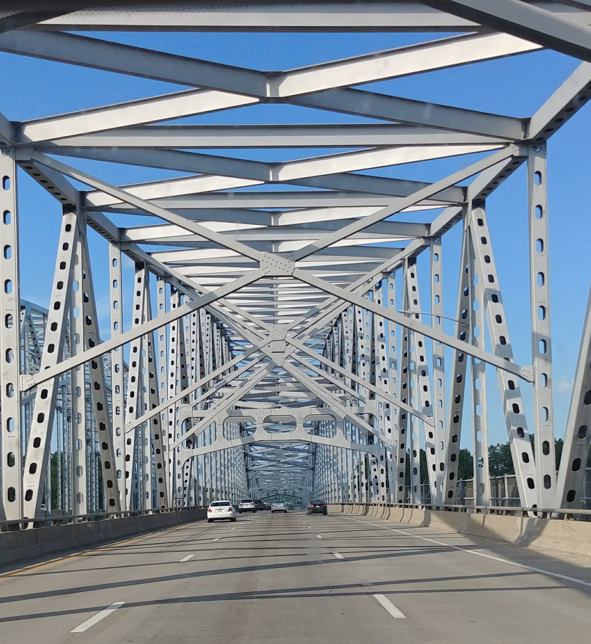 A steel truss bridge with intersecting beams spans a multi-lane road under a clear blue sky.