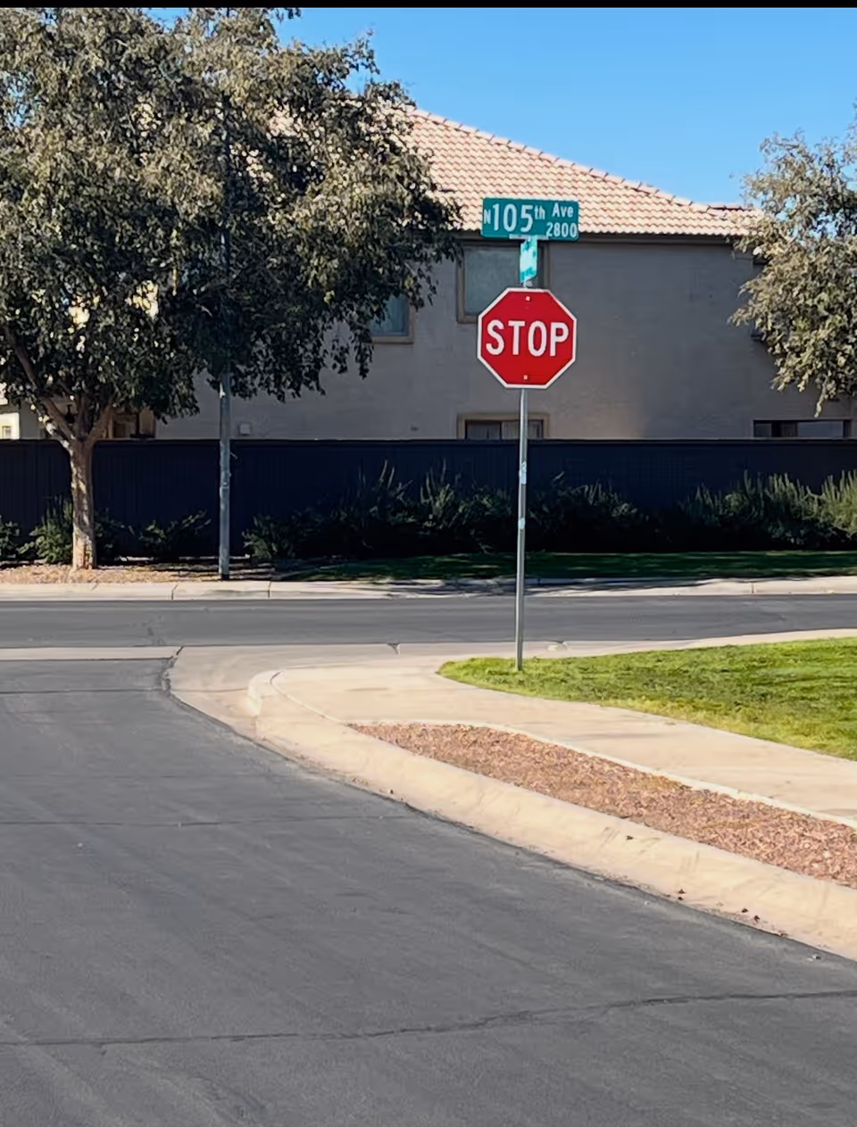Street view of a stop sign, curb, sidewalk, and building exterior with trees.