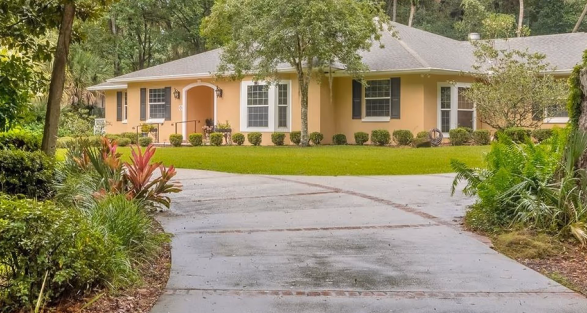 Yellow single-story assisted living building with front entrance, curved driveway, and manicured landscaping.