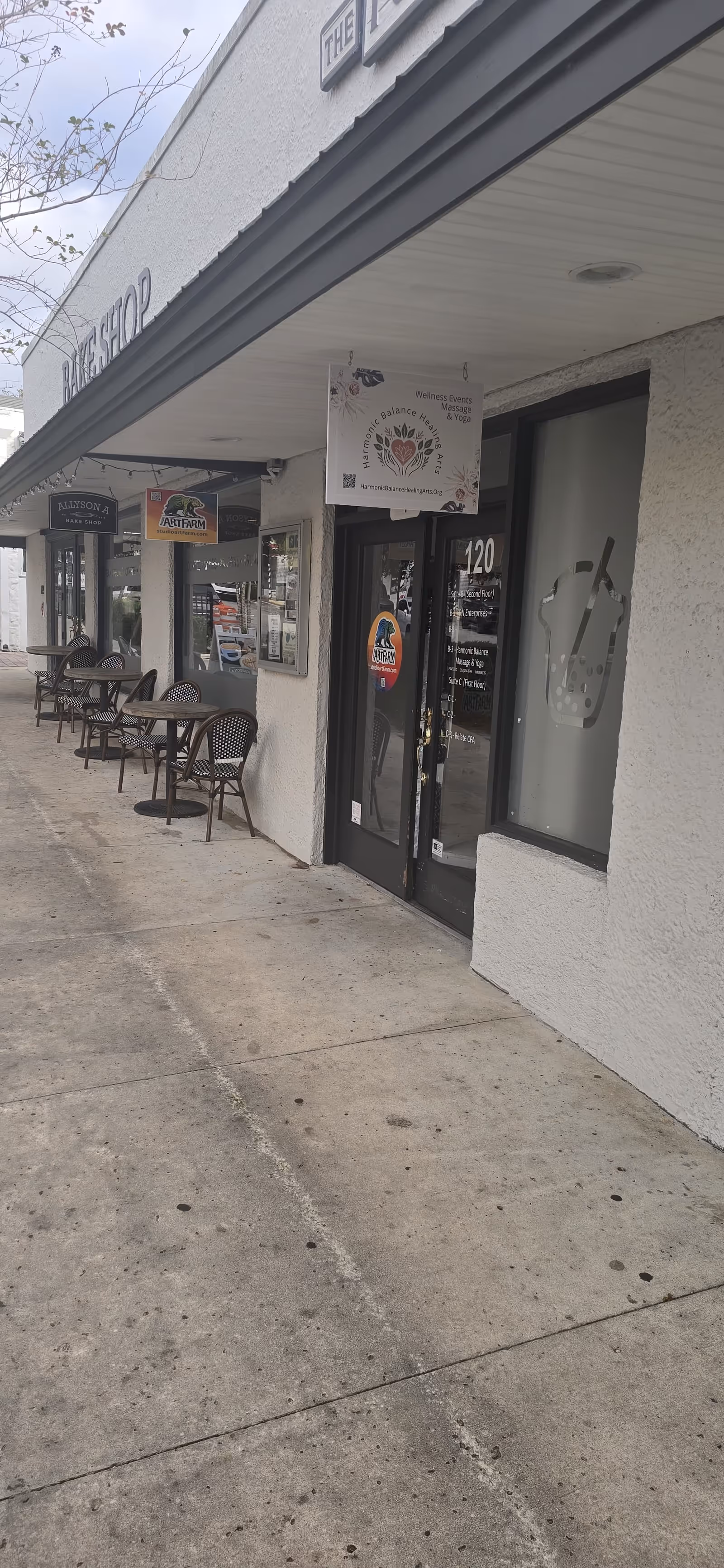 Exterior storefront with outdoor seating and signs along a shopping strip.