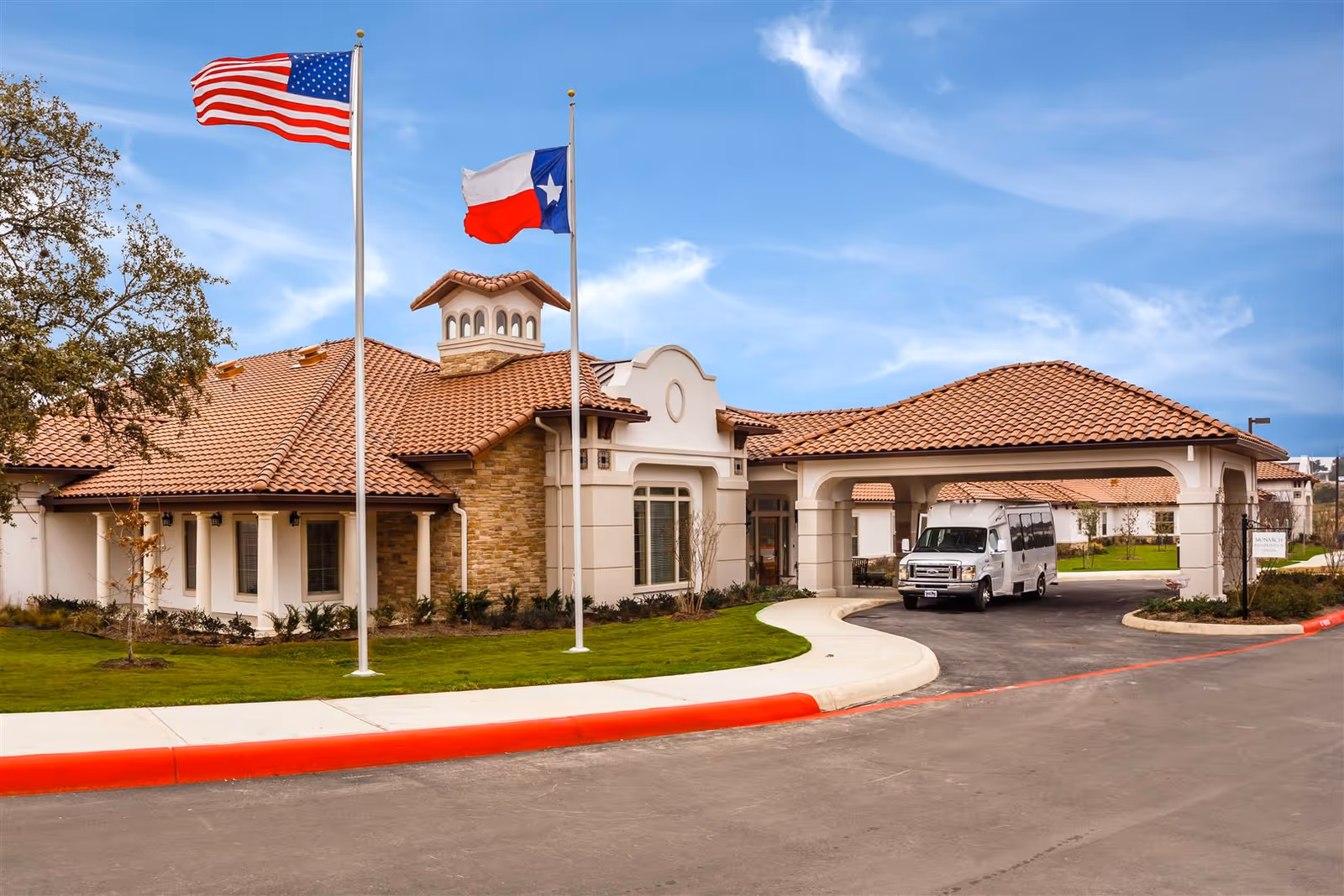 Exterior view of Coronado at Stone Oak, showing entrance, flagpoles, and a parked van.