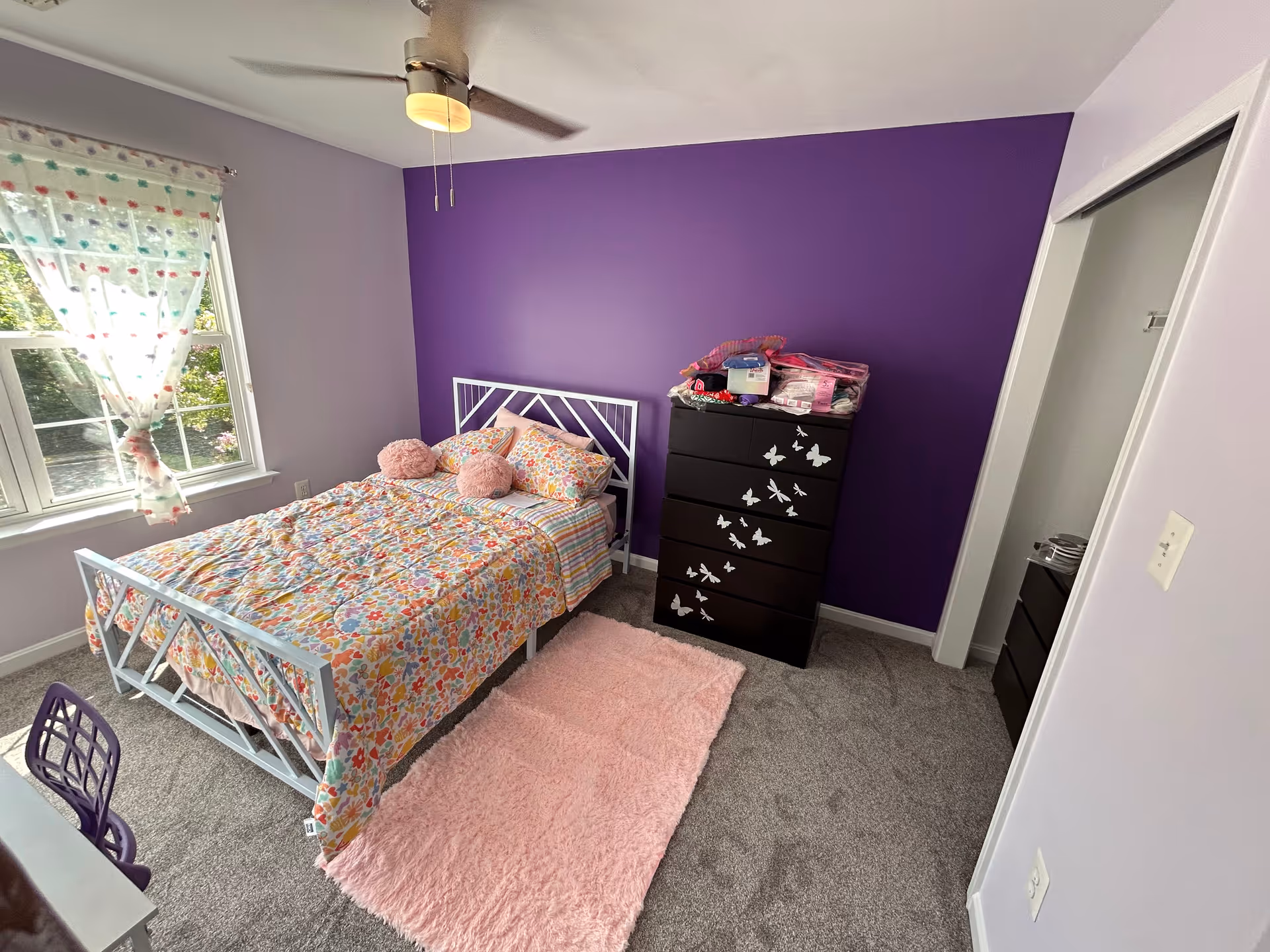 A cozy bedroom with a colorful quilted bed and purple accent wall.
