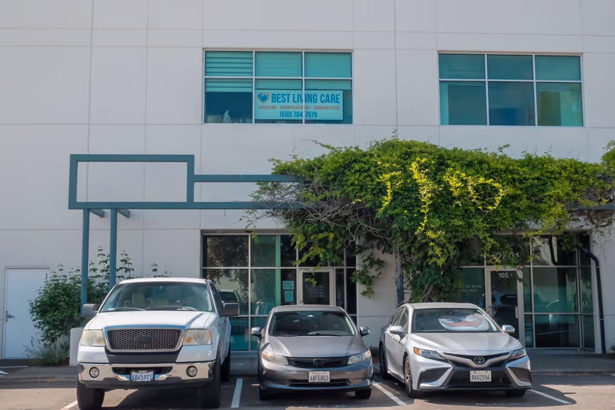 Exterior of a Best Living Care building with parked cars and greenery in front.