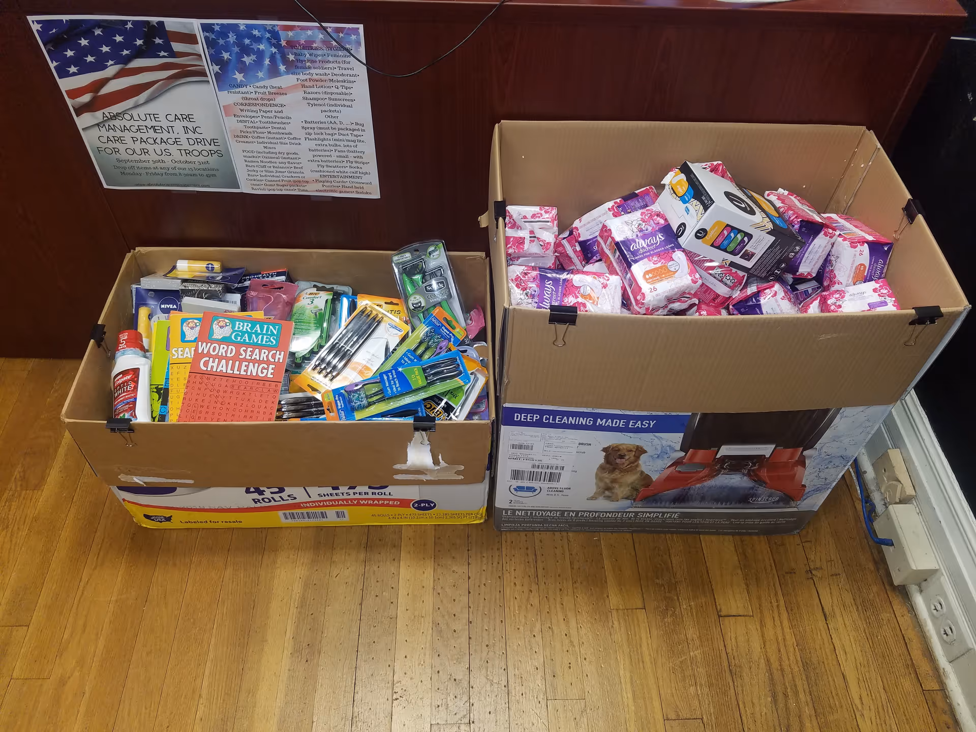 Two open cardboard boxes filled with donated supplies sit on a wooden floor.