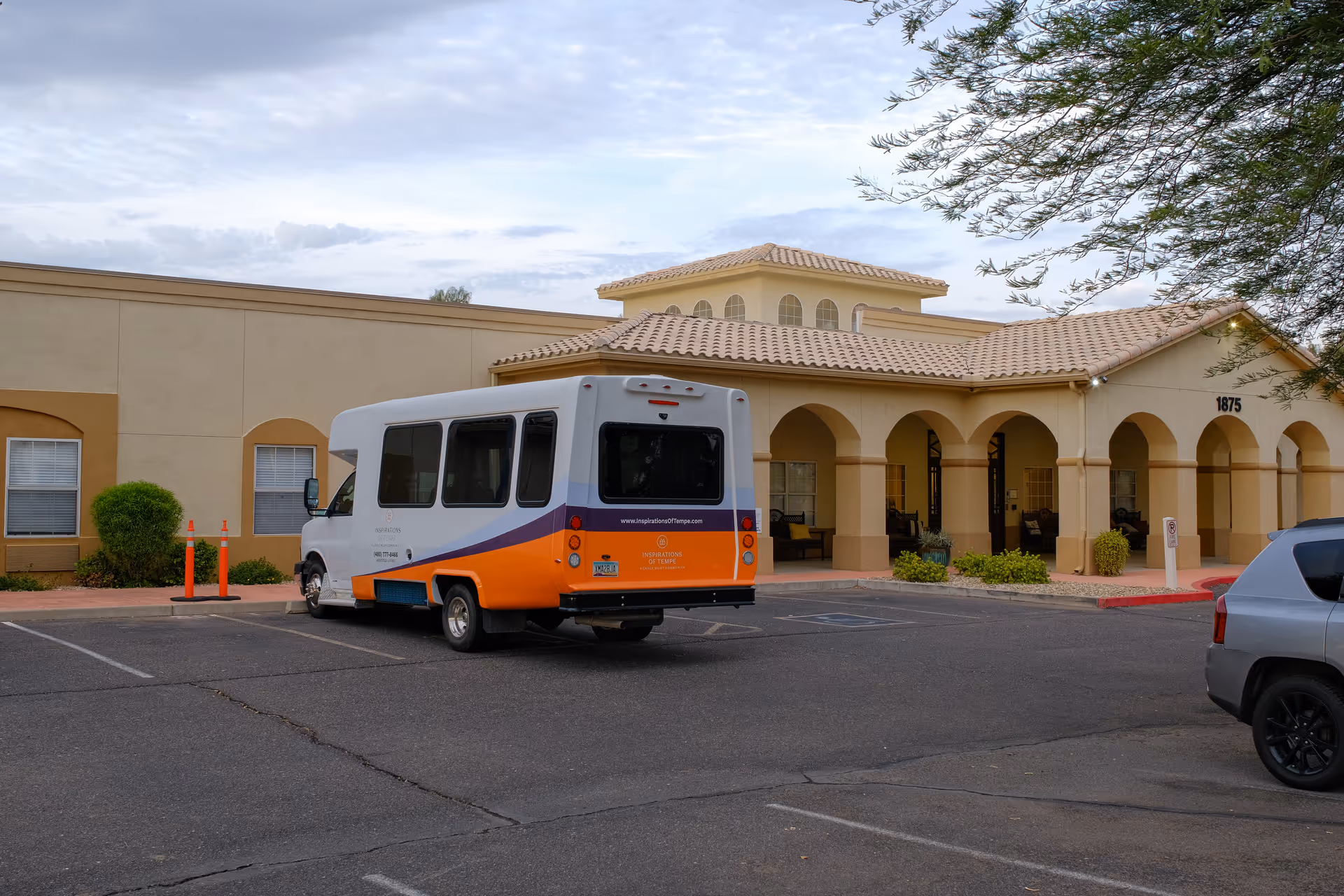 A white and orange shuttle bus parked in front of a beige senior living facility.