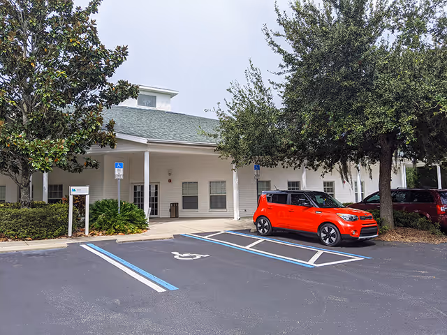Front view of a white senior care facility with a covered entrance and parking.