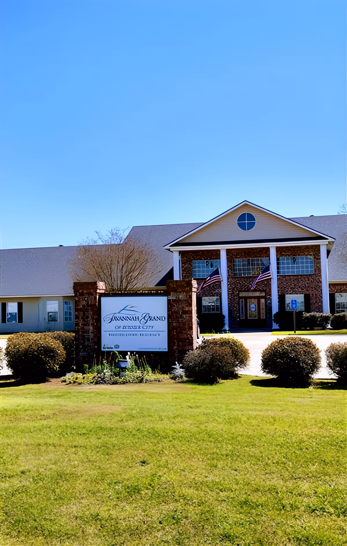 Front exterior of the Savannah Grand of West Monroe building showing the entrance with columns, American flags, and a lawn sign.