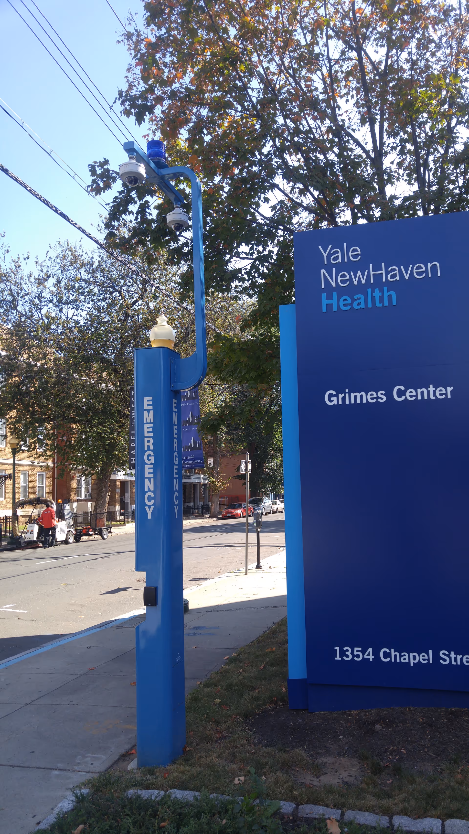 Blue Yale New Haven Health Grimes Center sign along the sidewalk with trees