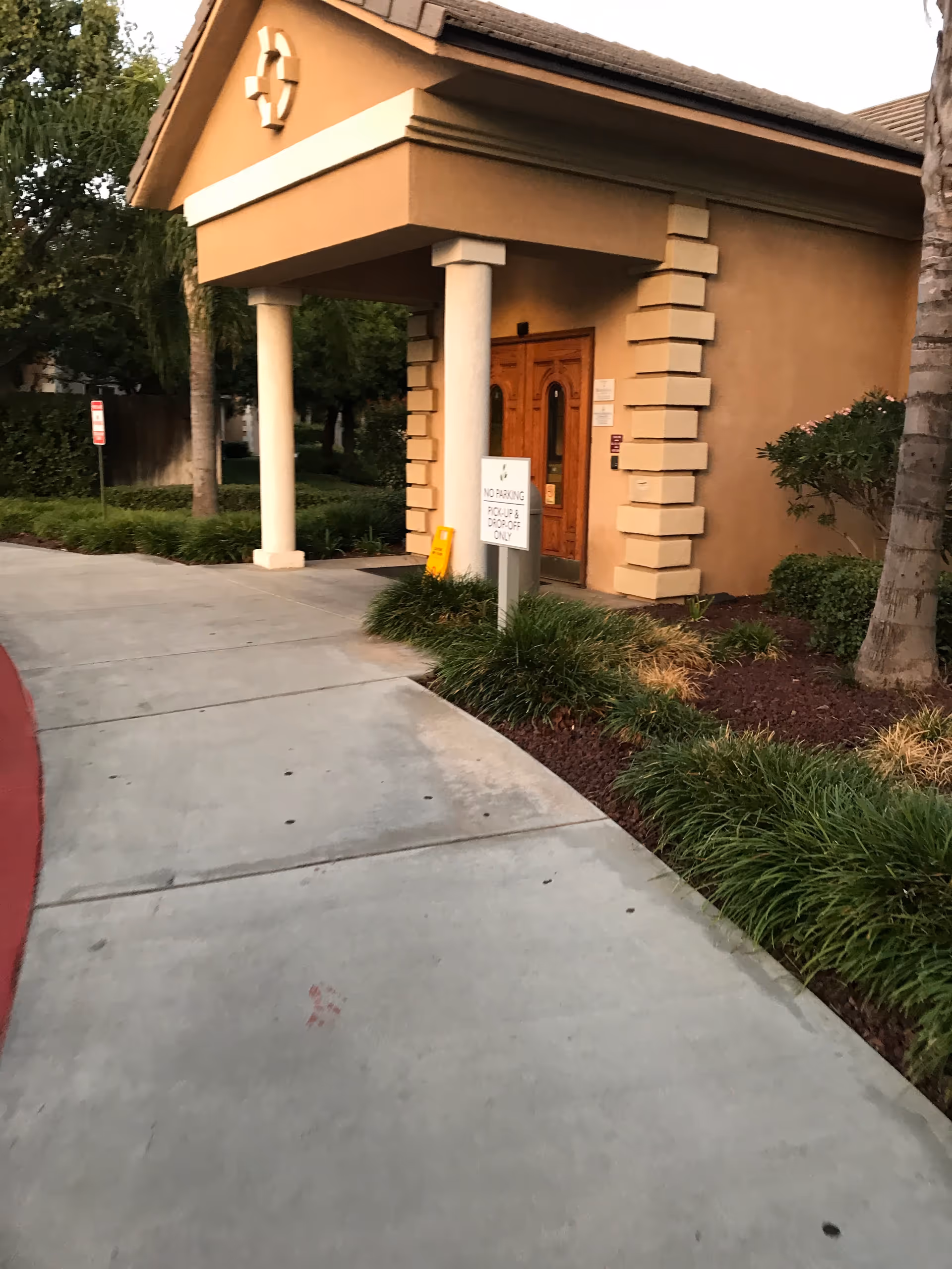 Beige building entrance with stone columns and a wooden door along a curved walkway.
