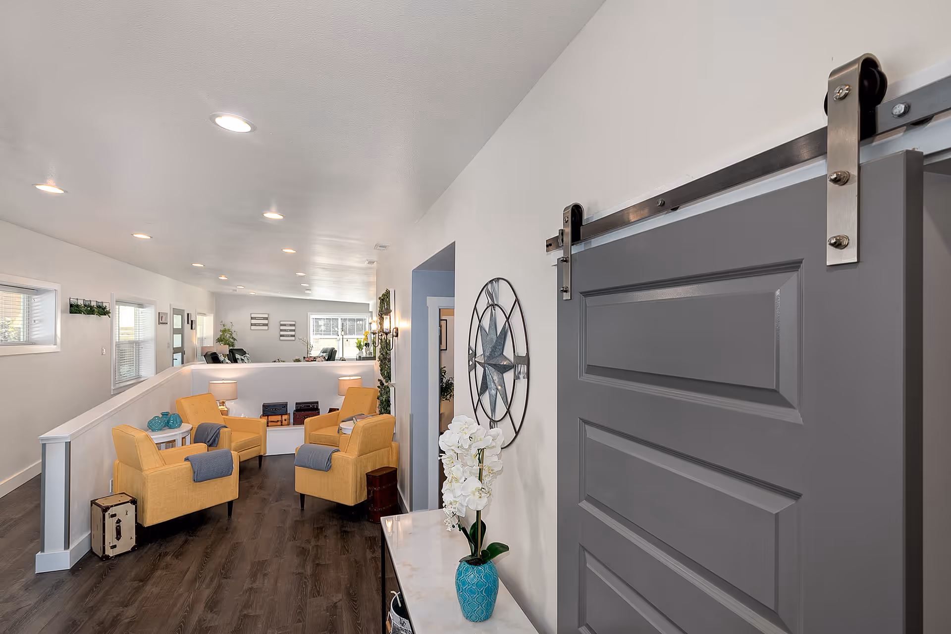 Bright senior living lounge with yellow chairs, white walls, and a gray sliding door.