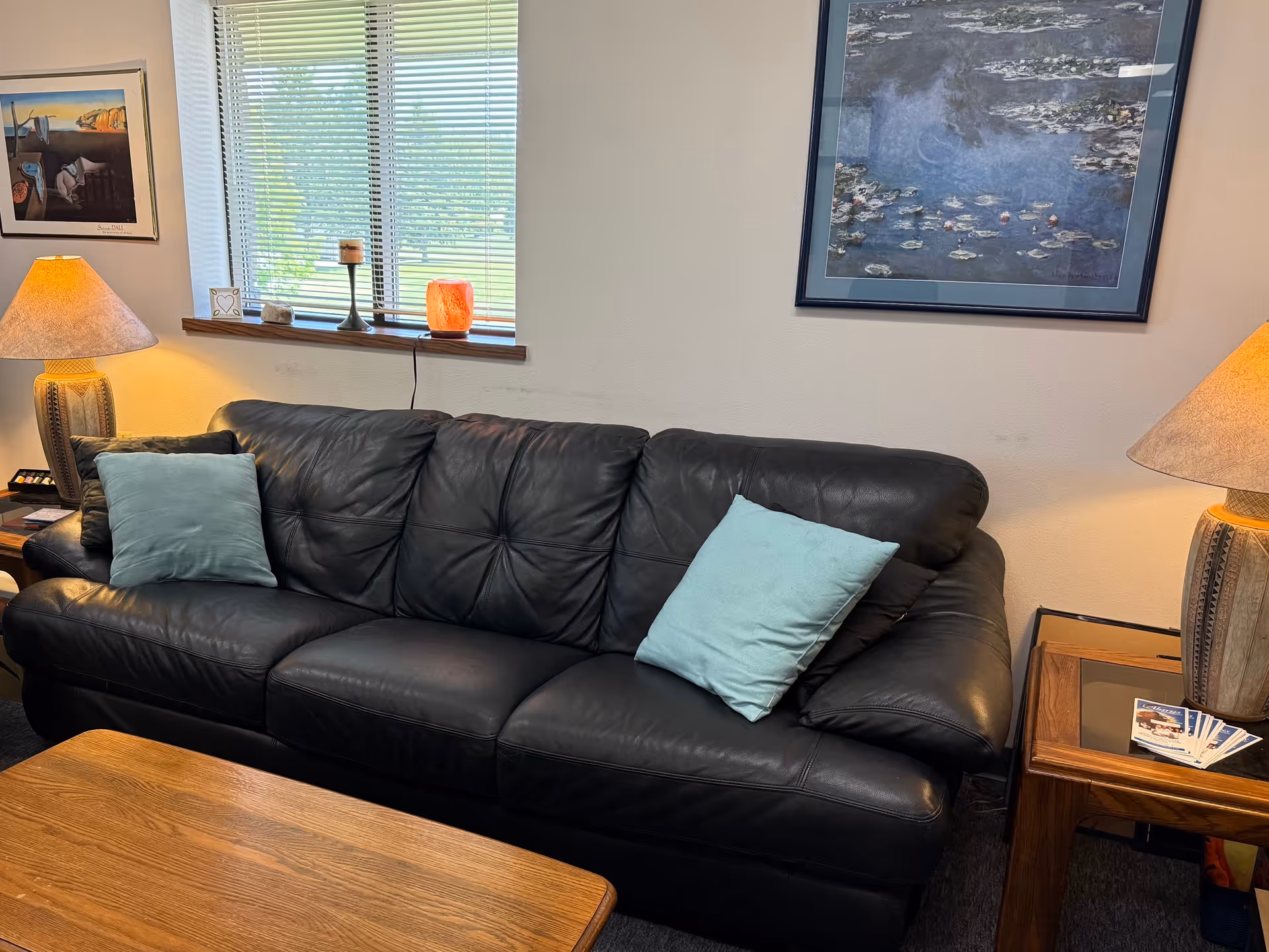 Cozy living room with black leather sofa, turquoise pillows, wood coffee table, and lamps.