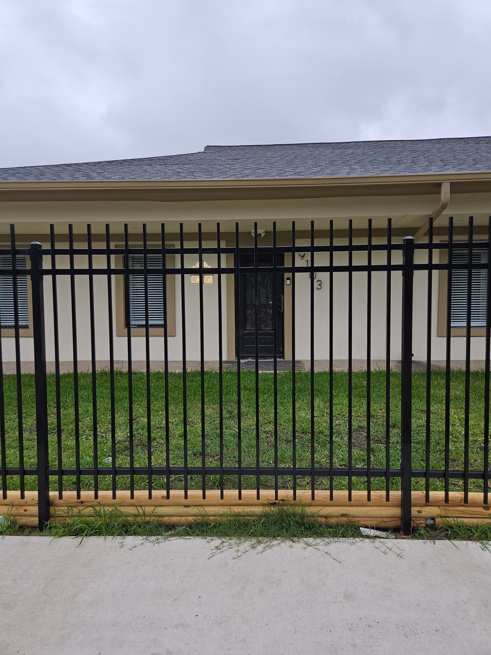 Front view of a single-story building behind a black metal fence and green lawn.