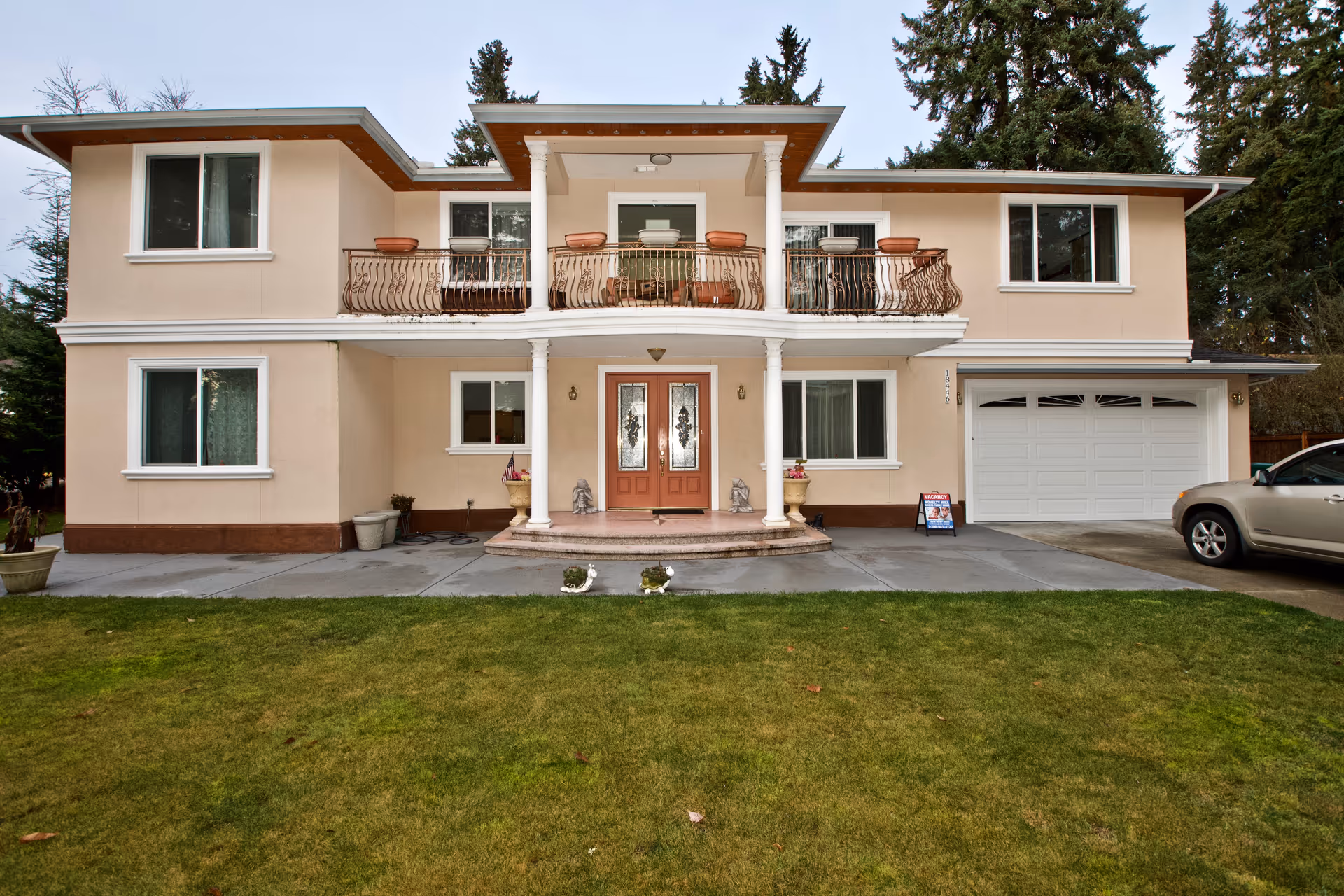 Two-story beige building with a central entrance, columns, and an upper balcony.