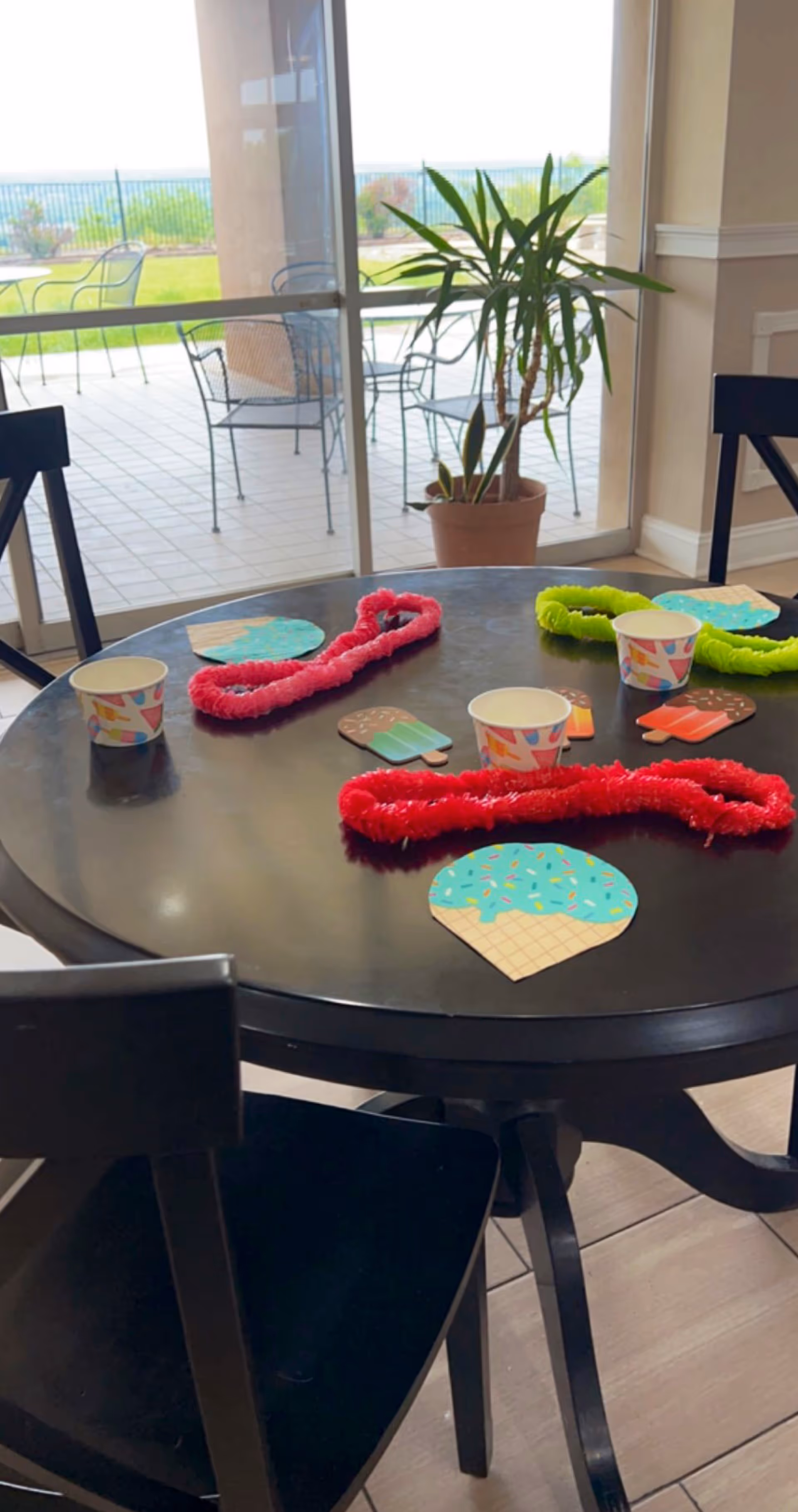 Indoor dining table with colorful party decorations, cups, and a patio view outside.