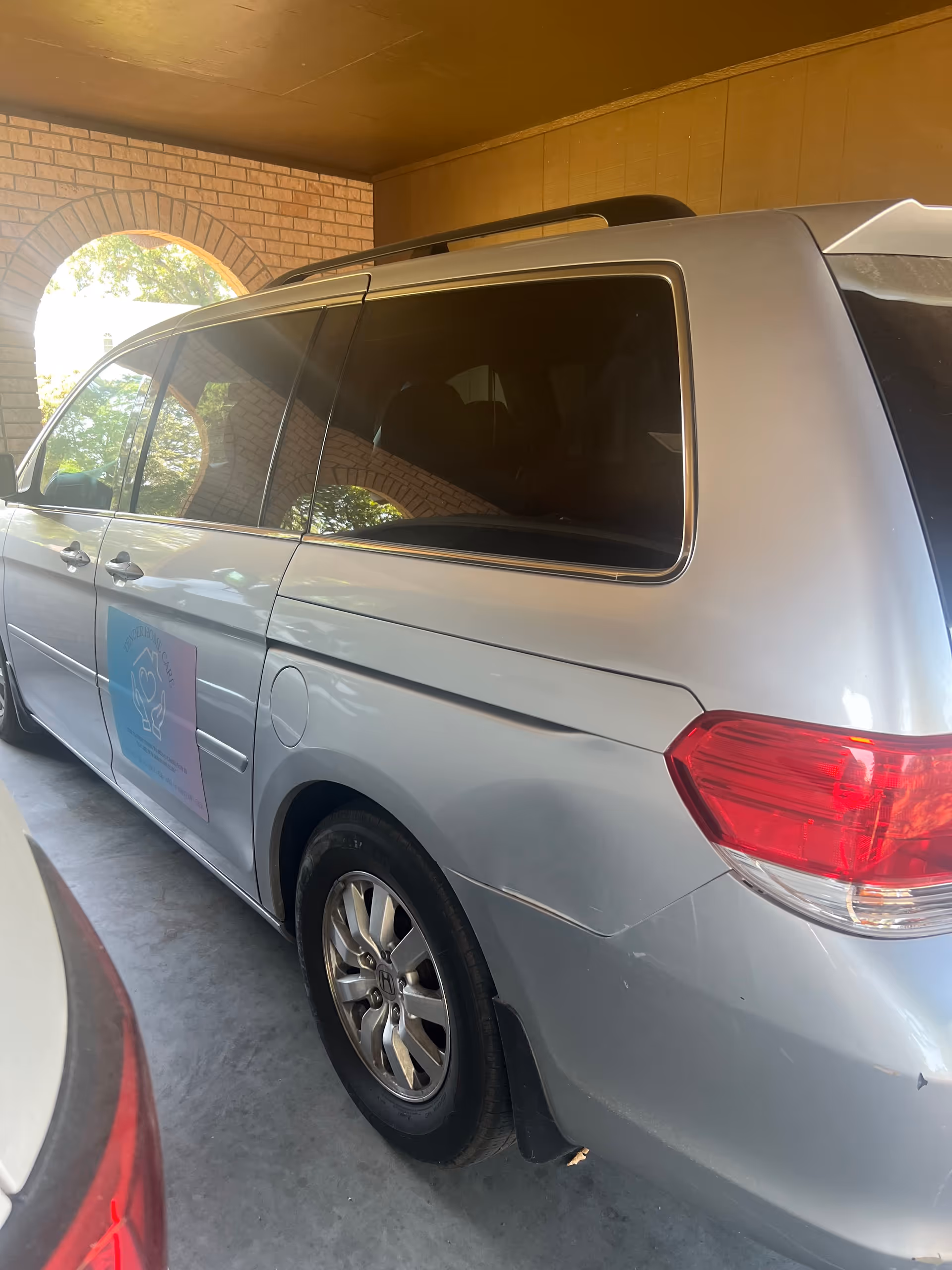 Silver van parked under a covered driveway beside a brick arch at Tender Home Care, LLC